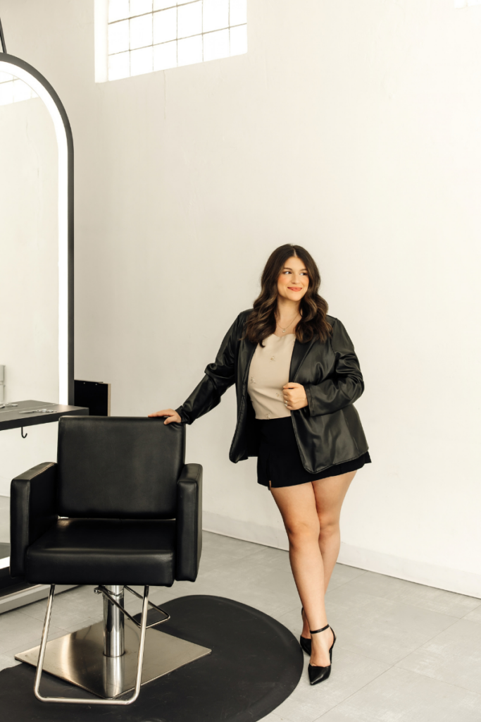 Portrait of stylist Gabbi Rumpza posing next to a modern lighted salon station.